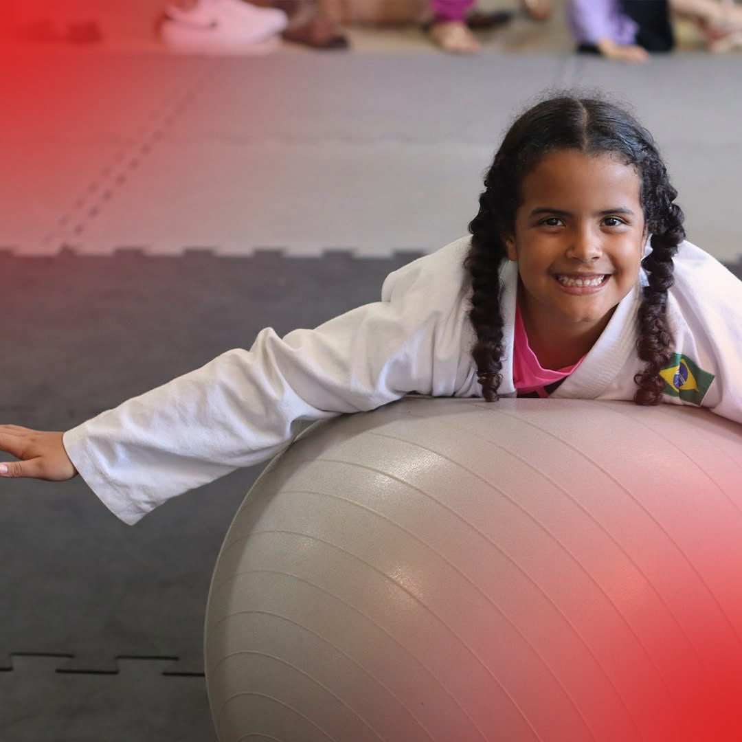Aluna kids sorrindo deitada sobre bola de pilates durante treino na Ollfight Anápolis